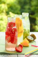 Trio of ice-cold fruit drinks on a wooden grey table on a summer garden background