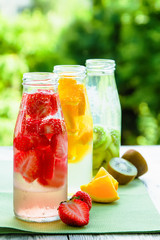 Trio of ice-cold fruit drinks on a wooden grey table on a summer garden background