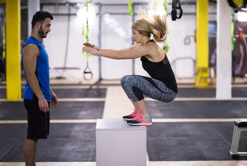 Tuinposter woman working out with personal trainer jumping on fit box © .shock