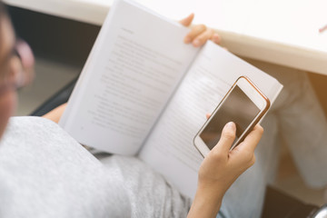 Close up Asian woman reading e-book on smartphone in the library..