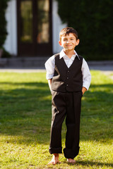 Cheerful boy in fashionable suit on green grass