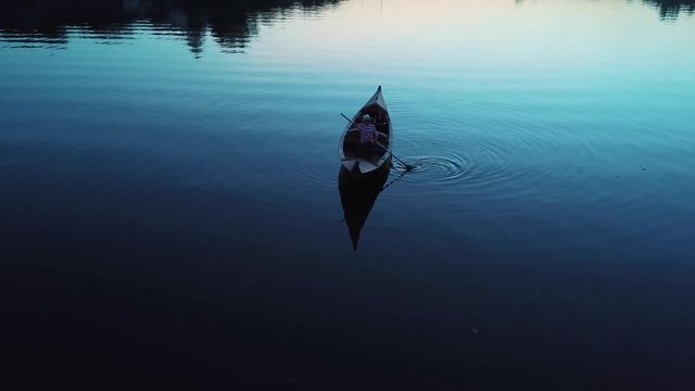 Aerial view of a young girl lying in a boat floating on a lake at night. Gondola with gondolier