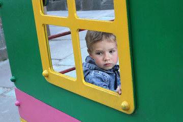 Children's phobias at the beginning of socialization. The kid looks sadly out the window. A sad child sits alone in a children's house on the playground.