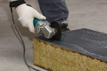 The hand of a worker in a glove cuts the building material with an angular grinding machine, creating sparks.