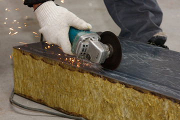 The hand of a worker in a glove cuts the building material with an angular grinding machine,...