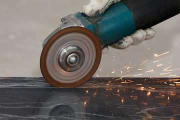 The hand of a worker in a glove cuts the building material with an angular grinding machine,...