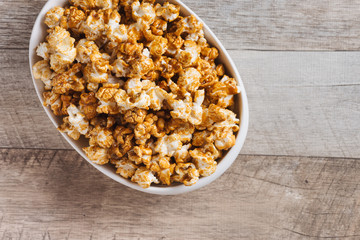 Caramel opcorn in bowl on the wooden table.