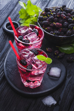 mulberry cocktail with ice and fresh mint on a black wooden table