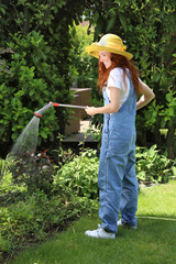 Hübsche rothaarige Frau steht in ihrem Garten und wässert ein Beet mit einer Handbrause