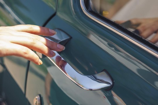 Close up woman hand holding a classic car door handle.