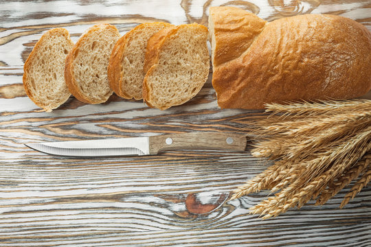 Knife sliced bread wheat ears on wooden surface