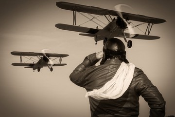 Porträt eines Vintage-Piloten mit Lederkappe, Schal und Fliegerbrille vor einem historischen Flugzeug-Doppeldecker - Porträt eines Mannes in historischer Pilotenkleidung - Vintage alter Bildstil