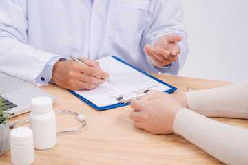 Doctor hand holding pen writing patient history list on note pad and talking to the patient about medication and treatment.