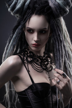 Portrait of woman with dreads and festive black gothic dress posing on dark background