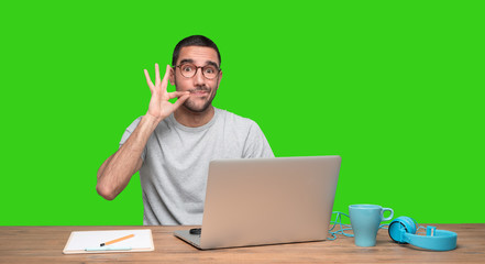 Confident young man sitting at his desk with a gesture of keeping a secret