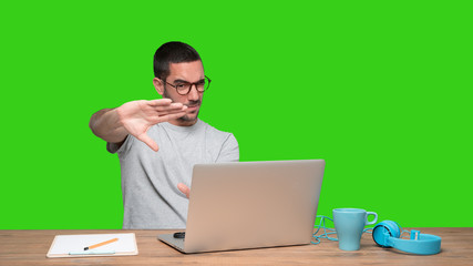 Concentrated young man sitting at his desk doing a gesture of focusing with his hands - Green background