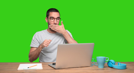 Shocked young man sitting at his desk - Green background