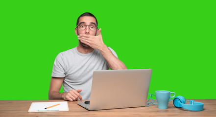 Shocked young man sitting at his desk - Green background