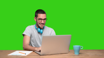 Fototapeta na wymiar Happy young man sitting at his desk and using a headphones - Green background