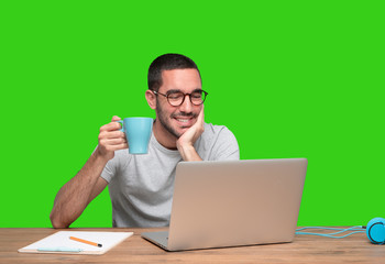 Young man sitting at his desk and drinking coffee - Green background