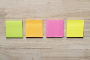 Set of green, orange, pink and yellow paper sticky notes glued on wooden table background