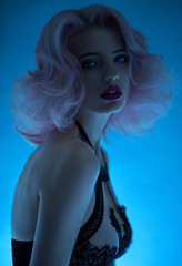 Portrait of woman with pastel pink hairstyle and fancy lingerie posing on blue background