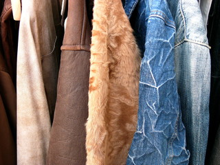 Herrenjacken aus Leder, Fell und verschiedenen Jeansstoffen vor einem Second Hand Laden im Sommer...