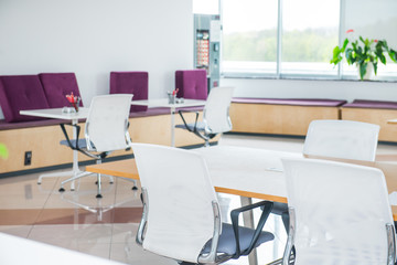 Interior of modern light empty open space office with big windows, table desks, chairs and green plants. Coworking workplace concept. Minimalism business style. Copy space. Selective focus.