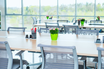 Interior of modern light empty open space office with big windows, table desks, chairs and green plants. Coworking workplace concept. Minimalism business style. Copy space. Selective focus.