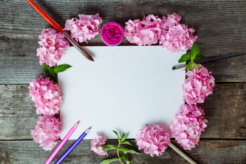 Top view Creative layout made of pink wisteria flowers, canvas blank, brushes, fuchsia color gouache paint, color pencils on the old wooden rustic table. Flat lay. Art concept. Copy space.