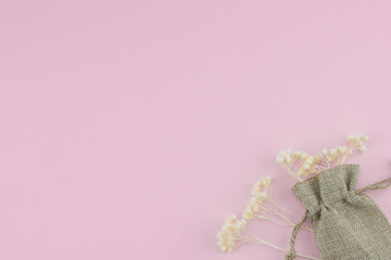 Obraz na płótnie Canvas Sackcloth bag with white dried flowers on pastel pink background with copy space 