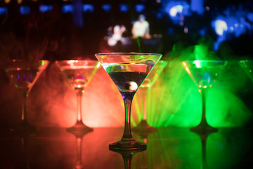 Several glasses of famous cocktail Martini, shot at a bar with dark toned foggy background and disco lights. Club drink concept
