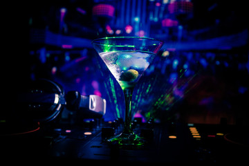 Glass with martini with olive inside on dj controller in night club. Dj Console with club drink at music party in nightclub with disco lights. Close up view