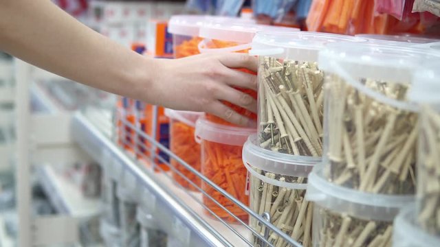 A young woman chooses a transparent container with orange corrugated plastic plugs in the store. She is preparing for repair or construction.