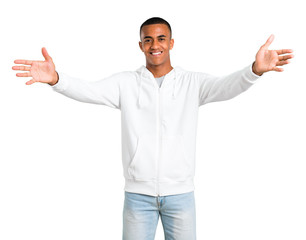 Dark-skinned young man with white sweatshirt presenting and inviting to come with hand. Happy that you came on isolated white background