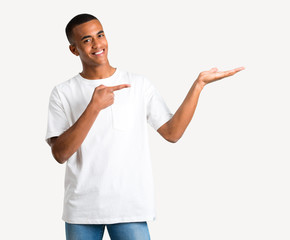 Young african american man holding copyspace imaginary on the palm to insert an ad on isolated...