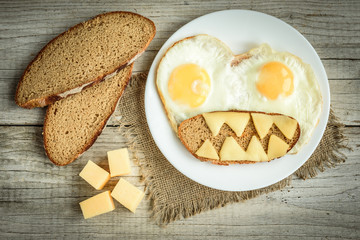Top view of fried egg angry face with bread and cheese on white plate on wooden table. Healthy breakfast.