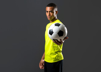Soccer player man with dark skinned playing catching a ball with his hands on dark background