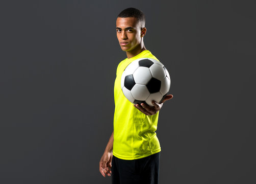Soccer player man with dark skinned playing catching a ball with his hands on dark background