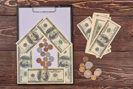 Black clipboard with blank paper sheet, american dollars cash. Top view, flat lay. Wooden desk background.