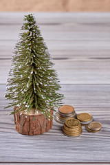 Tiny artificial christmas tree and columns of coins. Close up. Wooden desk background.