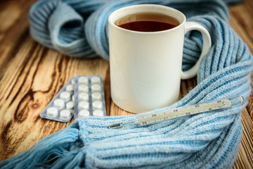 Thermometer, blue scarf and tea on wooden table. Disease and healthcare background.