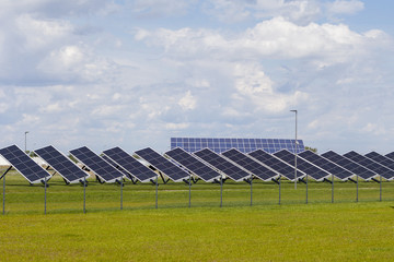Power plant solar panels on a green field under a blue sky with fluffy clouds