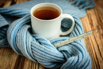 Thermometer, blue scarf and tea on wooden table. Disease and healthcare background.