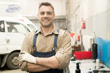 Portrait of young attractive Caucasian male automotive technician standing in repair workshop and smiling at camera happily