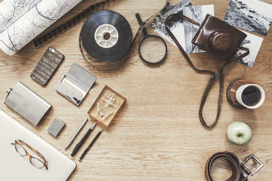 Stylish composition of flat lay on wooden desk with laptop, map, cup of coffee, croissant, phone, notebook, camera and office accessories. Creative desk of photographer. Copy space for inscription.