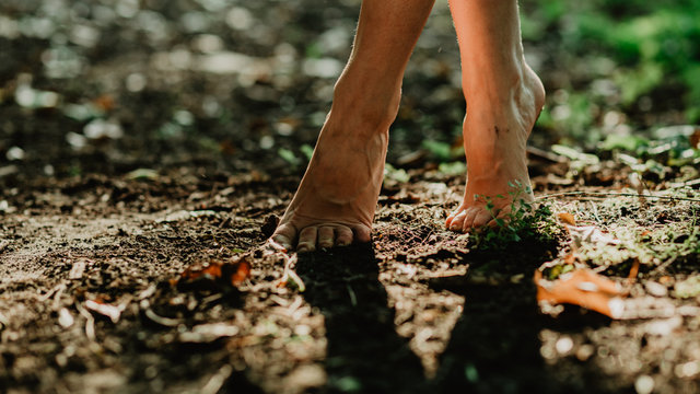 Young girl walking barefoot in the secret botanic garden. Close up image of female bare feet touching soil and green grass in the forest. 