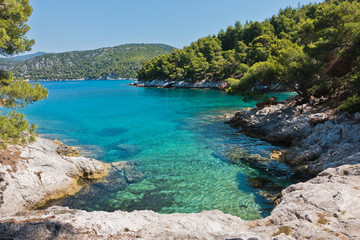 Naklejka na ściany i meble Small lagoon with pine trees and rocks over crystal clear turquoise water near Cape Amarandos at Skopelos island, Greece