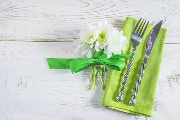 Festive table setting with bouquet of white chrysanths flowers and beautiful cutlery on green napkin on white paint wooden background