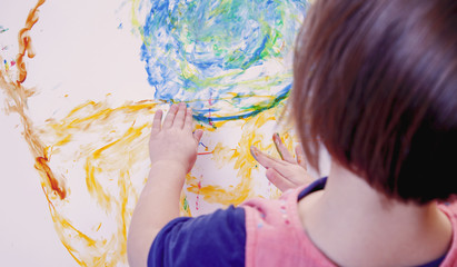 Little cute child girl holding a paint brush and painting on a white wall background